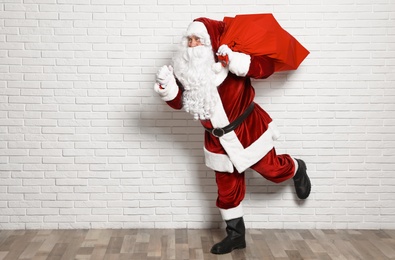 Authentic Santa Claus with bag full of gifts against white brick wall. Space for text