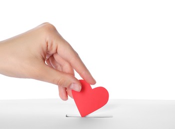 Photo of Woman putting red heart into slot of donation box against white background, closeup