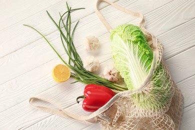 Photo of Fresh ripe Chinese cabbage and other vegetables in net bag on white wooden table, top view