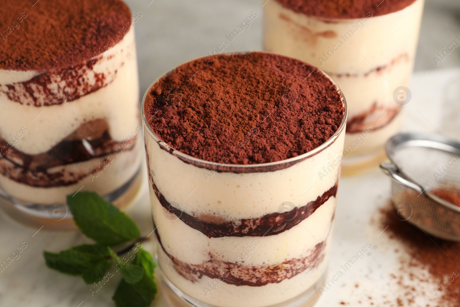 Photo of Delicious tiramisu in glasses and mint on table, closeup