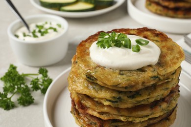 Delicious zucchini pancakes with sour cream served on light grey table, closeup