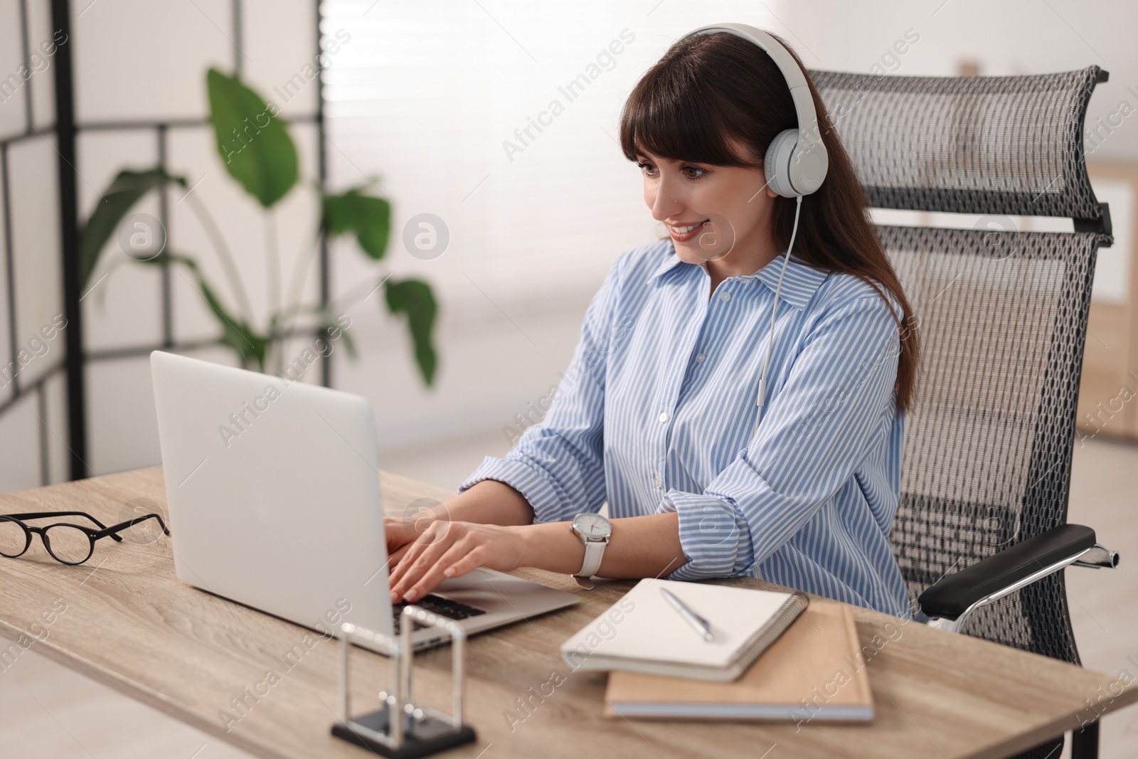 Photo of Woman in headphones watching webinar at wooden table in office