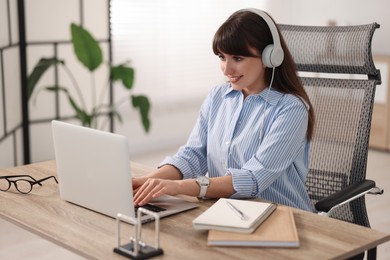 Photo of Woman in headphones watching webinar at wooden table in office