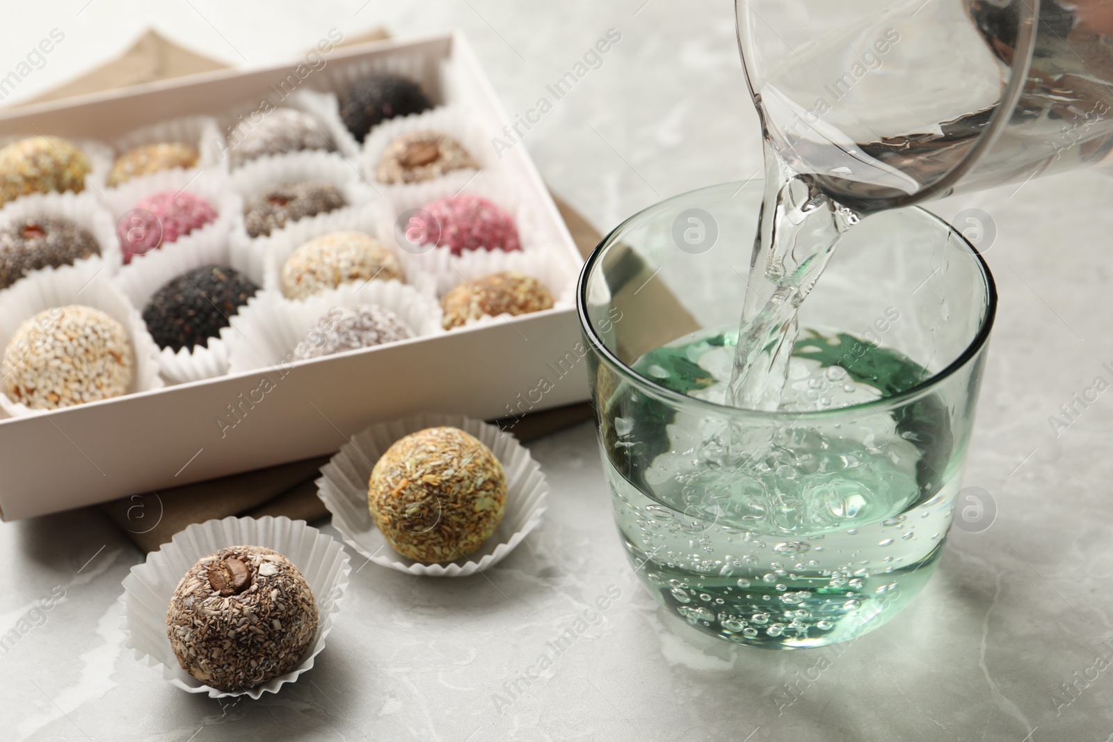 Photo of Pouring water into glass and delicious vegan candy balls at light grey marble table