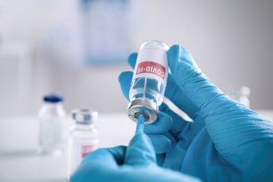 Photo of Doctor filling syringe with vaccine against Covid-19 indoors, closeup