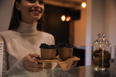 Photo of Young woman holding takeaway coffee cups in cafe, focus on cardboard holder