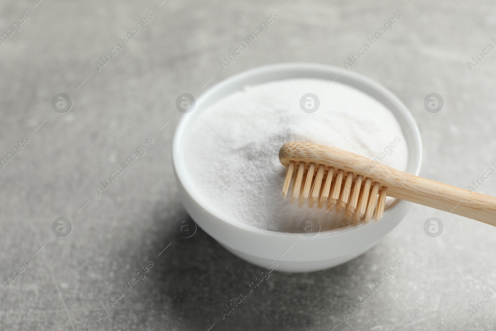 Photo of Bamboo toothbrush and bowl of baking soda on grey table, closeup. Space for text