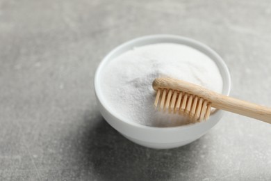 Bamboo toothbrush and bowl of baking soda on grey table, closeup. Space for text