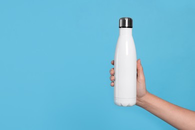 Photo of Woman holding thermo bottle on light blue background, closeup. Space for text
