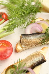 Photo of Delicious sandwiches with sprats, pickled cucumber, onion and dill served on plate, closeup