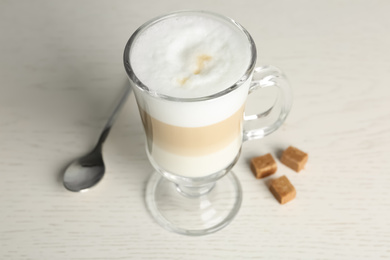 Photo of Delicious latte macchiato and sugar cubes on white table, closeup