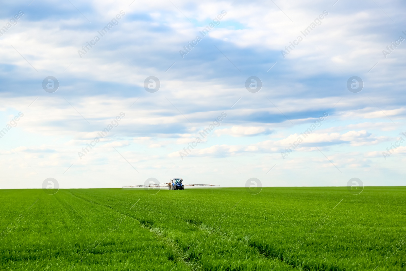 Photo of Tractor spraying pesticide in field on spring day. Agricultural industry