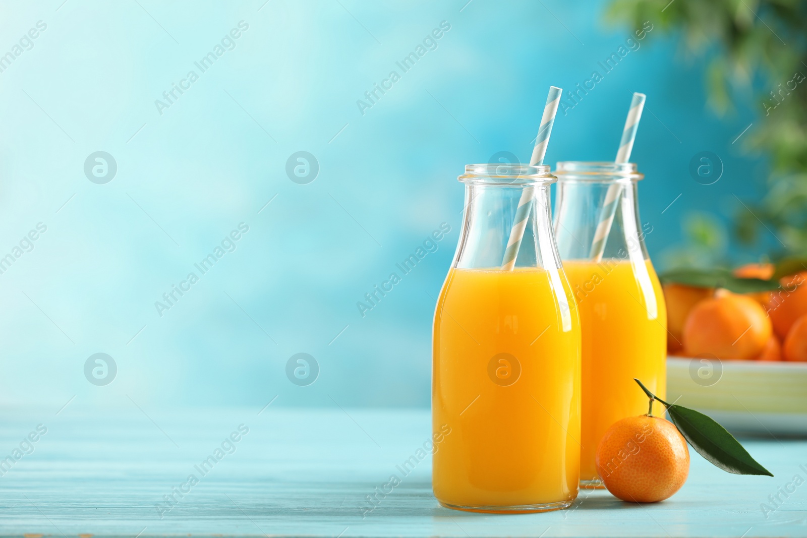 Photo of Bottles of fresh tangerine juice on blue wooden background. Space for text