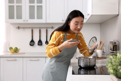 Photo of Beautiful woman cooking and smelling soup in kitchen. Space for text