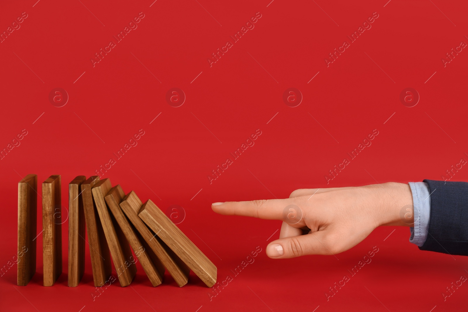 Photo of Woman causing chain reaction by pushing domino tile on red background, closeup. Space for text