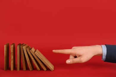 Photo of Woman causing chain reaction by pushing domino tile on red background, closeup. Space for text