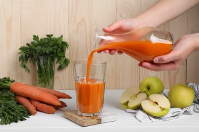 Woman pouring carrot juice from jug into glass at white wooden table, closeup