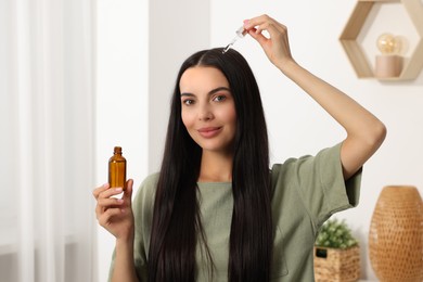 Beautiful woman applying hair serum in room. Cosmetic product