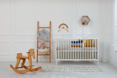 Cute baby room interior with comfortable crib and wooden rocking horse