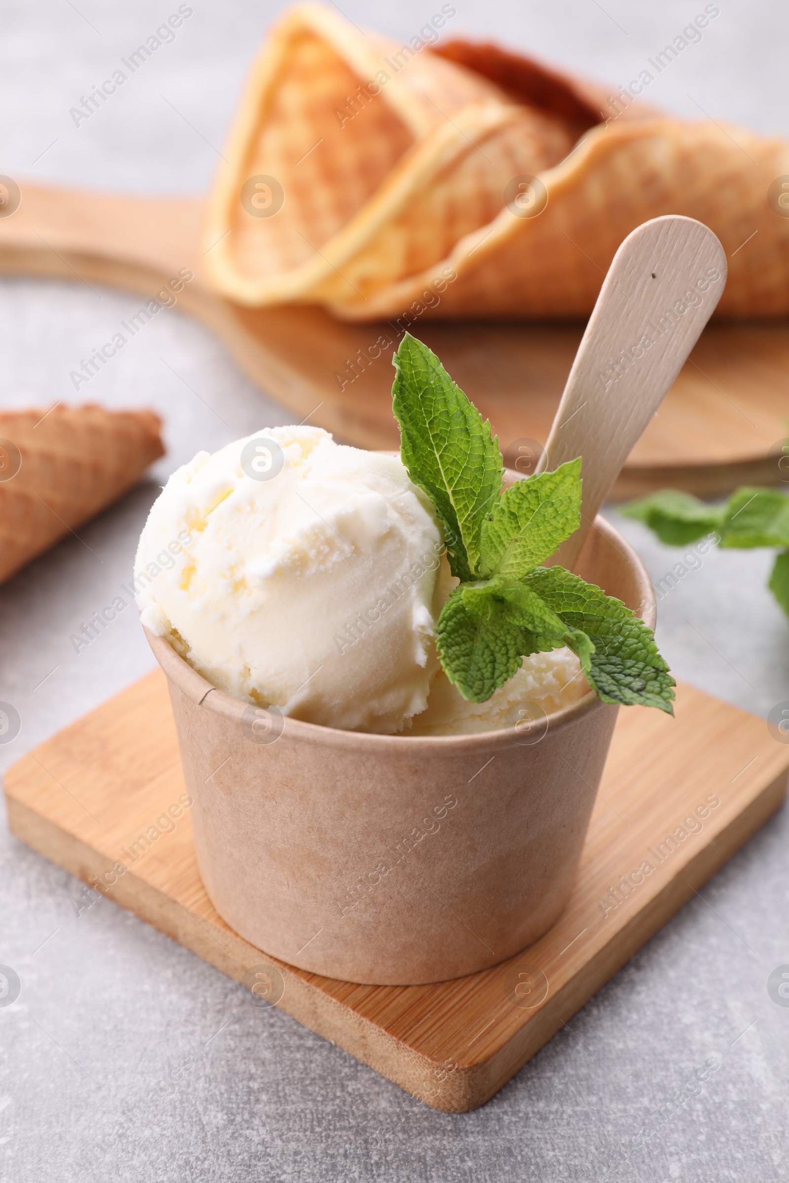 Photo of Delicious vanilla ice cream with mint in paper cup on light grey table, closeup