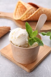 Delicious vanilla ice cream with mint in paper cup on light grey table, closeup