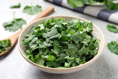 Cut fresh green cilantro in bowl on light grey marble table, closeup