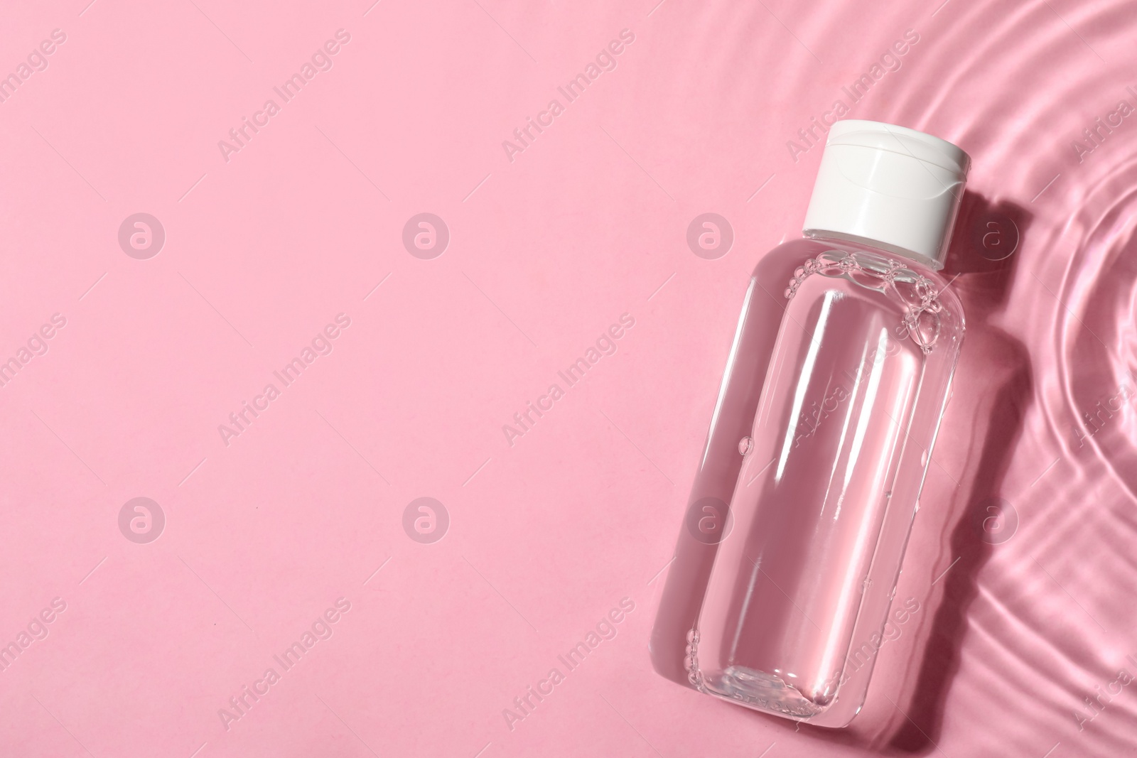 Photo of Wet bottle of micellar water on pink background, top view. Space for text