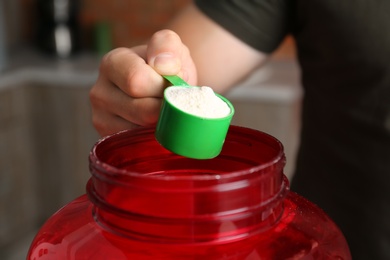Photo of Man holding scoop with protein powder over jar in kitchen, closeup