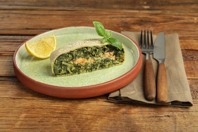 Photo of Piece of tasty strudel with salmon and spinach served on wooden table