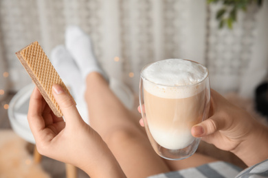 Woman having delicious wafer and coffee for breakfast indoors, closeup