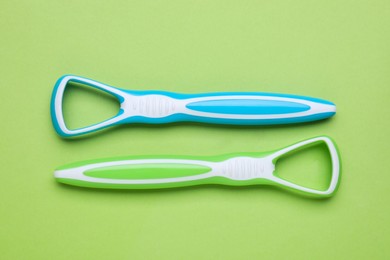 Photo of Colorful tongue cleaners on light green background, flat lay