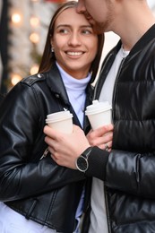 Photo of Lovely young couple with cups of coffee enjoying time together outdoors, closeup. Romantic date