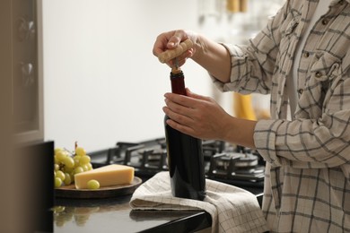 Photo of Woman opening wine bottle with corkscrew at countertop indoors, closeup