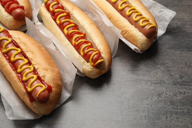 Photo of Delicious hot dogs with mustard and ketchup on grey table, closeup. Space for text