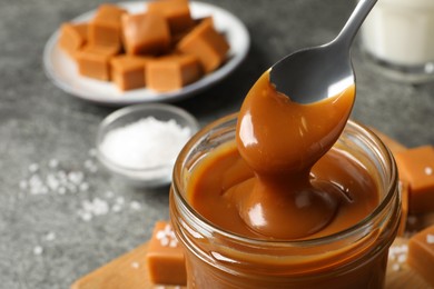 Photo of Taking yummy salted caramel with spoon from glass jar at table, closeup. Space for text