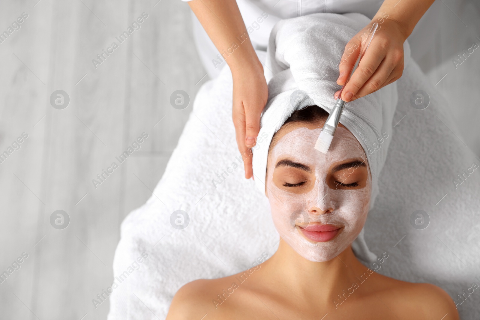 Photo of Cosmetologist applying mask on woman's face in spa salon, top view. Space for text