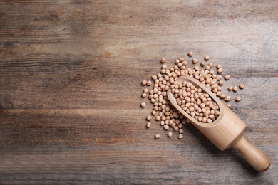 Photo of Scoop with chickpeas on wooden table, flat lay. space for text