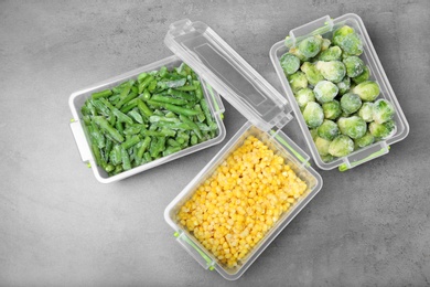 Plastic containers with frozen vegetables on grey background, top view