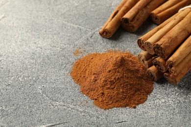Photo of Cinnamon powder and sticks on grey table, closeup. Space for text