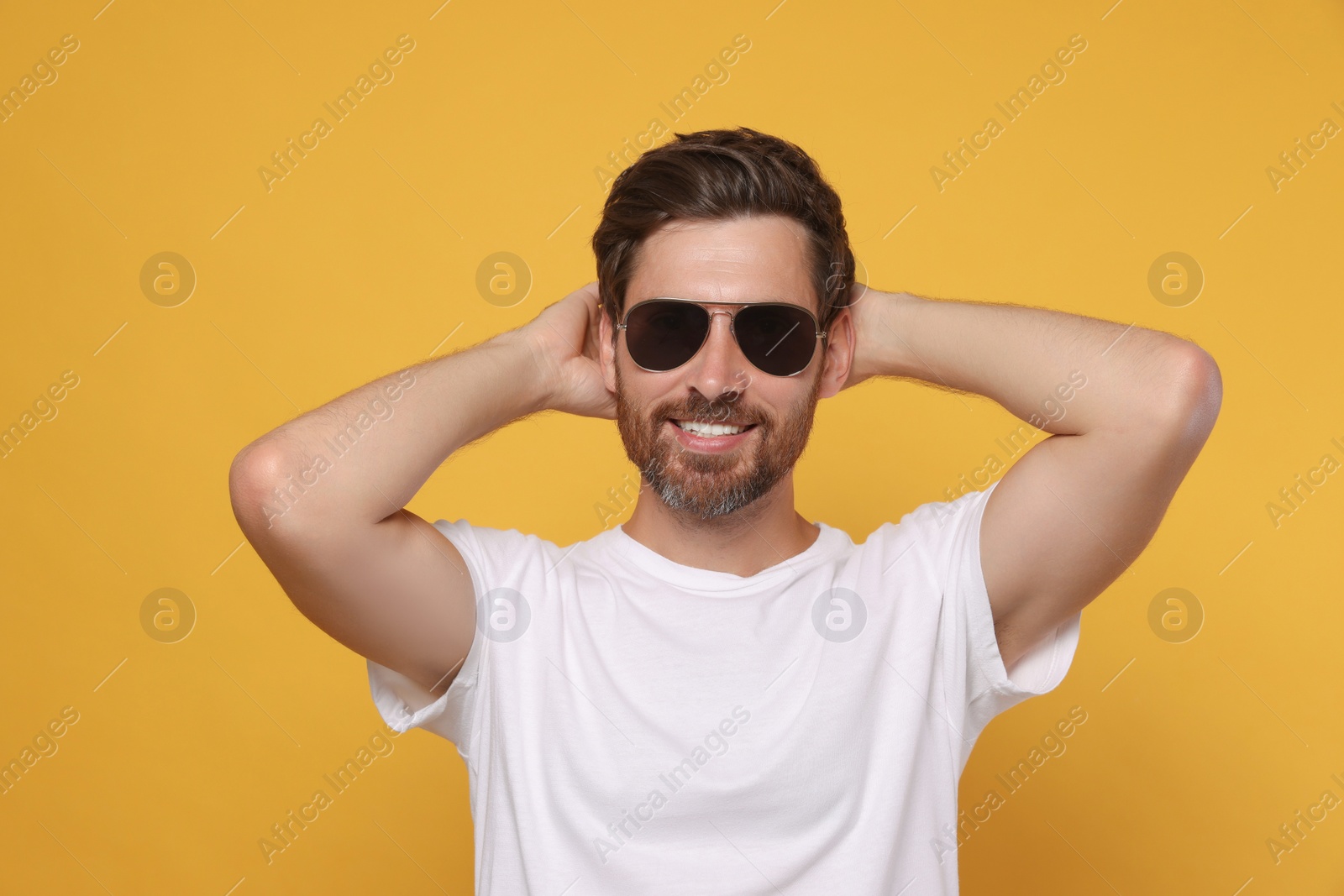 Photo of Portrait of smiling bearded man with stylish sunglasses on orange background