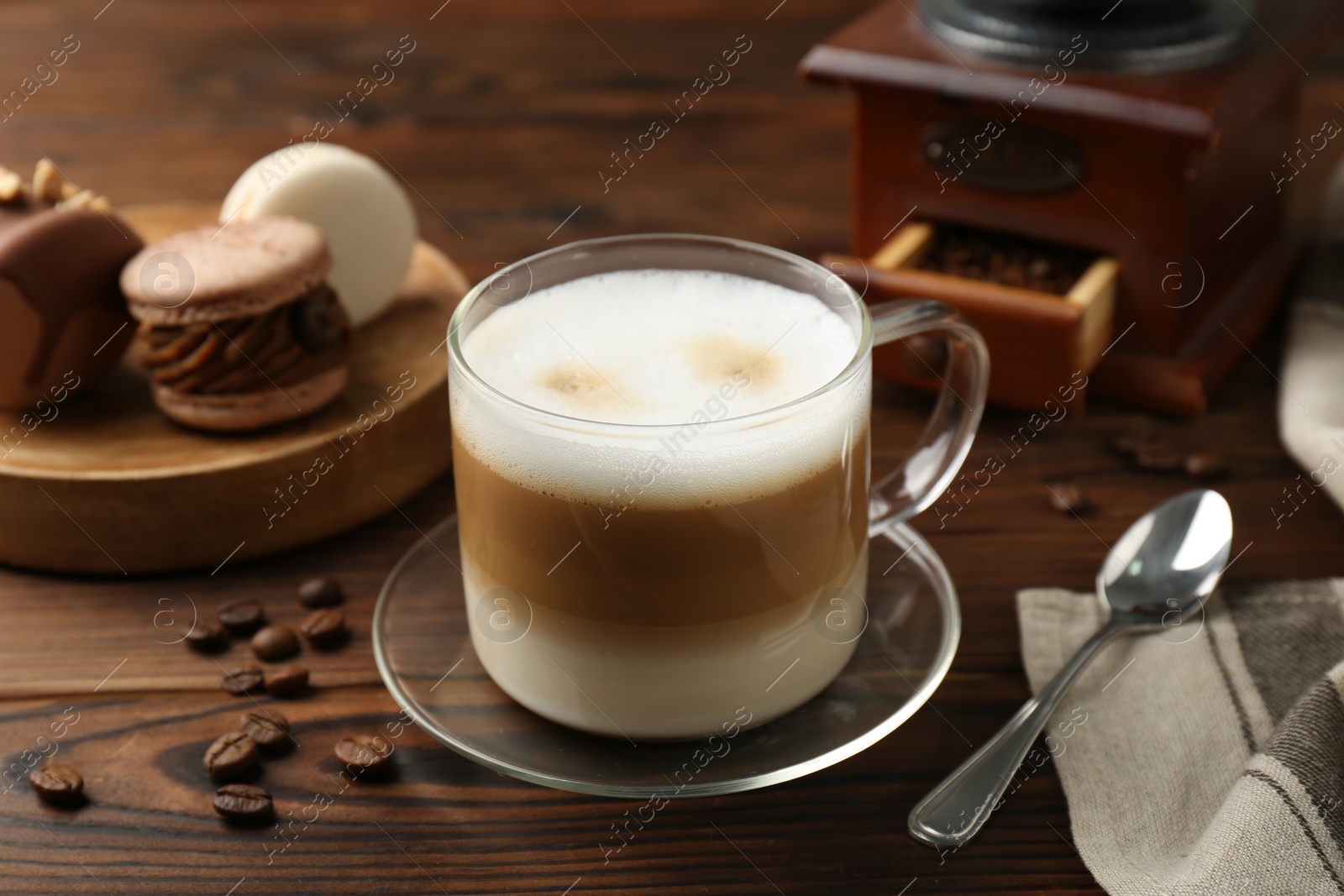 Photo of Aromatic coffee in cup, beans, spoon and macarons on wooden table