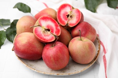 Photo of Tasty apples with red pulp and leaves on white tiled table