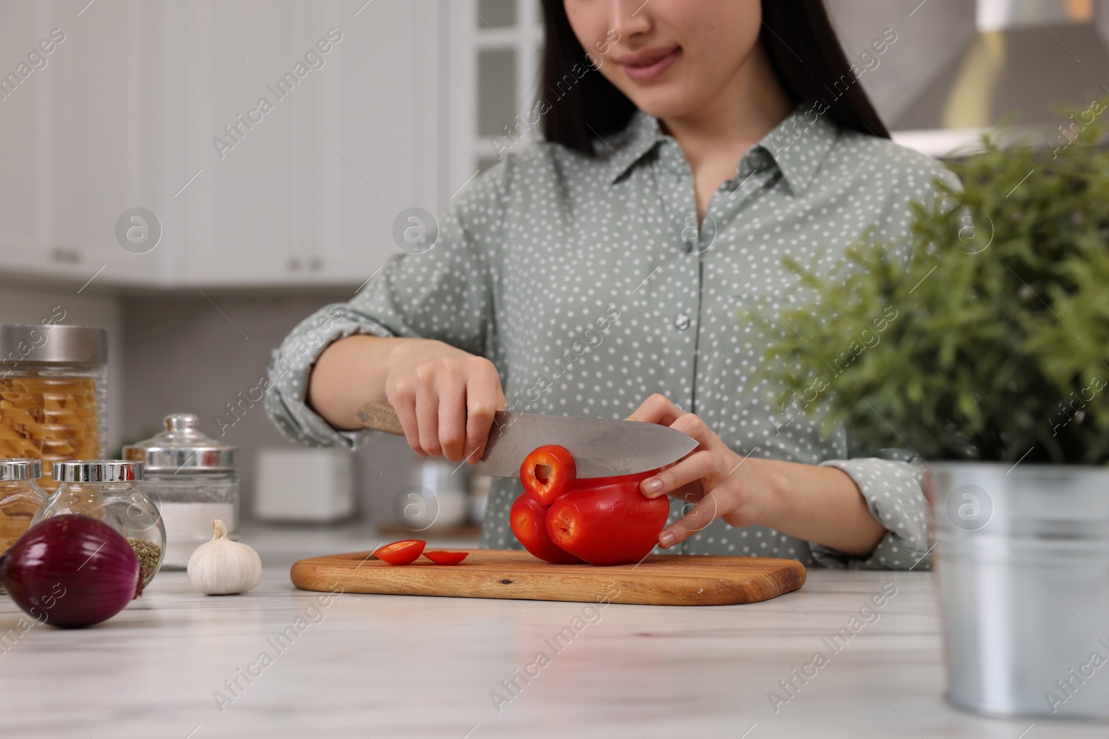 Photo of Cooking process. Woman cutting bell pepper at white countertop in kitchen, closeup