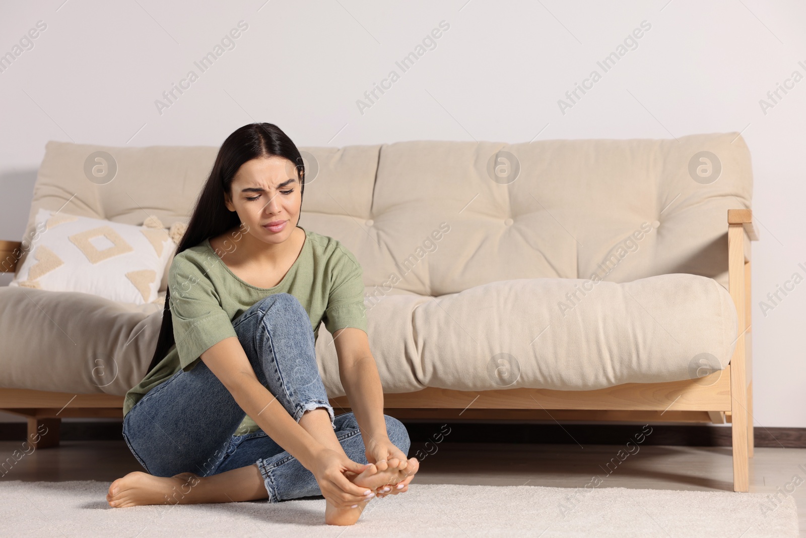 Photo of Woman rubbing sore foot on floor at home, space for text