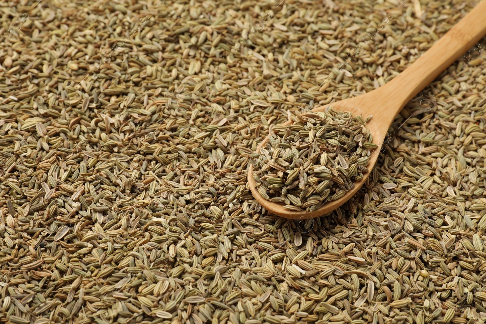 Photo of Heap of fennel seeds and wooden spoon as background, closeup. Space for text