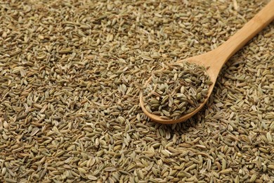 Heap of fennel seeds and wooden spoon as background, closeup. Space for text