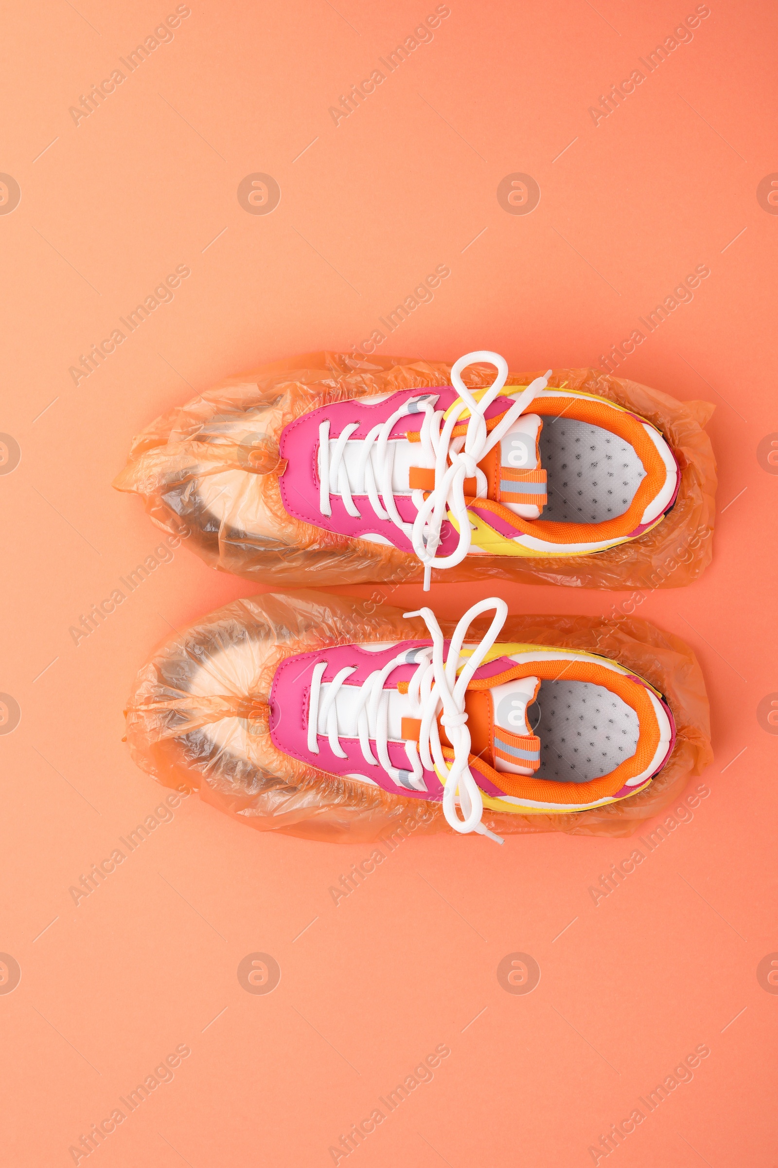 Photo of Women's sneakers in shoe covers on coral background, top view