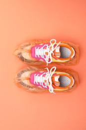 Photo of Women's sneakers in shoe covers on coral background, top view