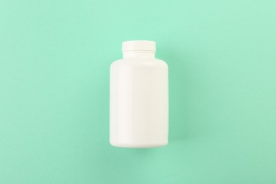 Blank white pill bottle on turquoise background, top view. Space for text