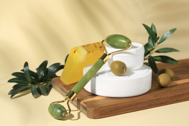Cosmetic products, olives and jade roller on beige background